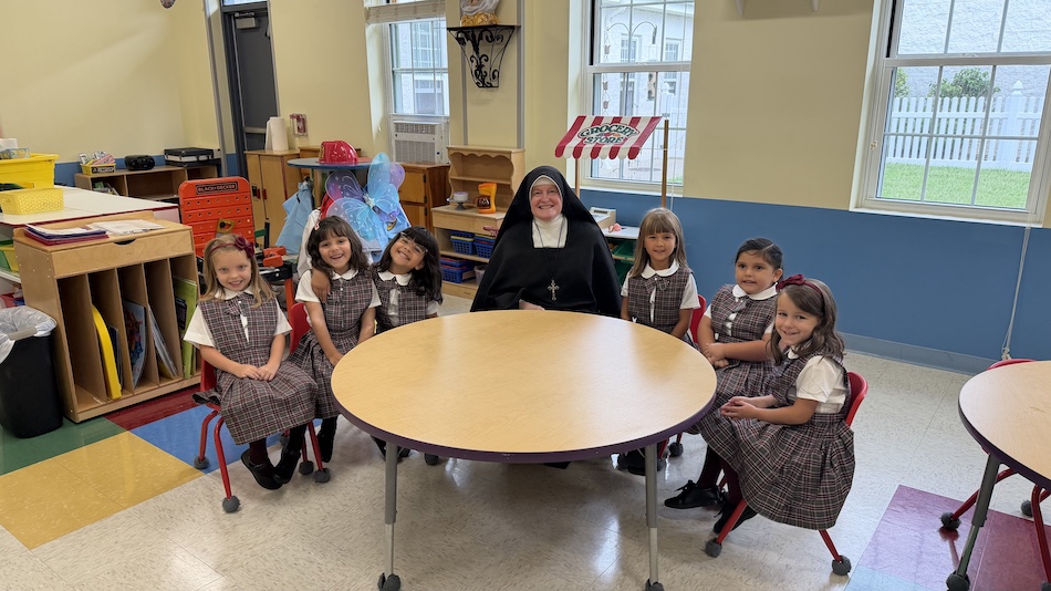 A Sister with the kindergarten students at their classroom table