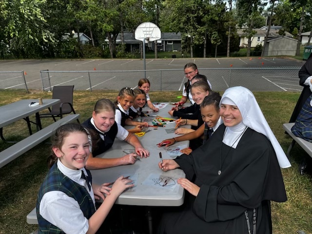 A Sister doing crafts with students at an outdoor picnic table